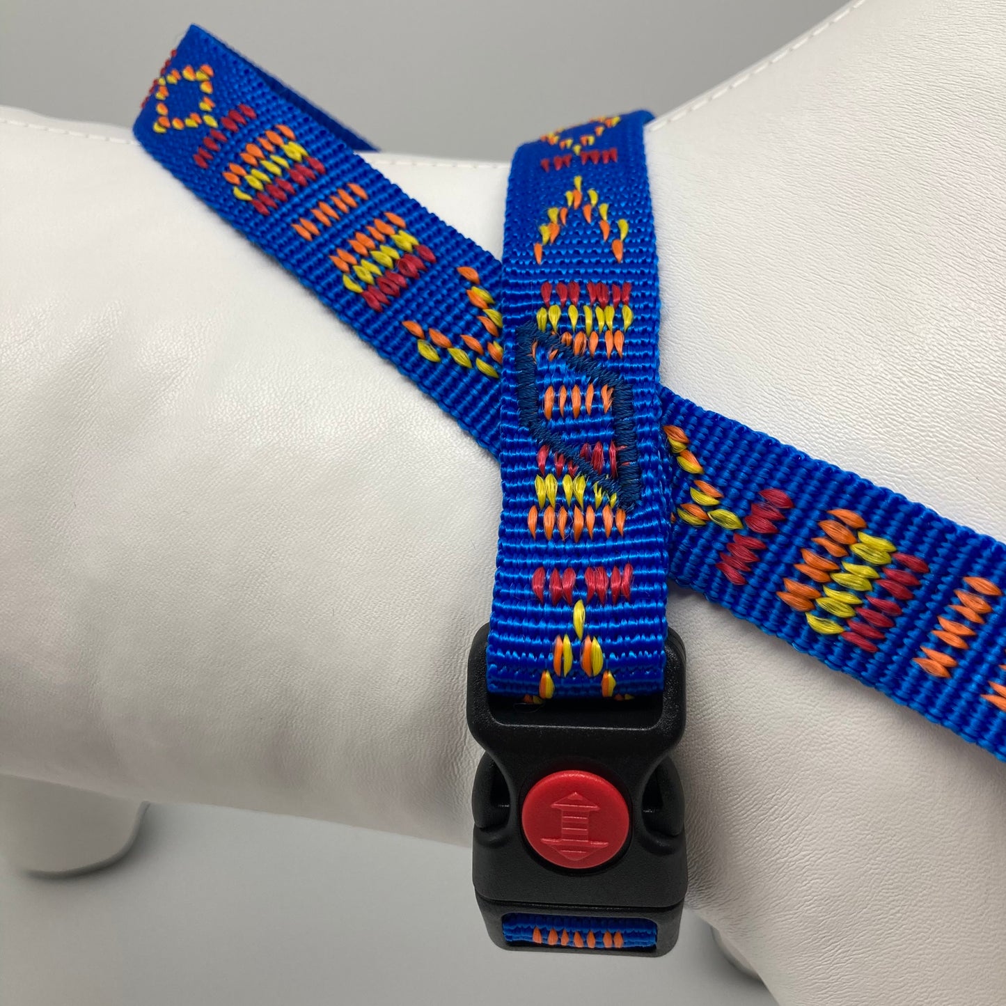 blue Stitch (blue fabric with print in 3 colors, red, yellow and orange) harness displayed on a stuffed toy (dog), around the torso, showing the black lock and the loop on the back
