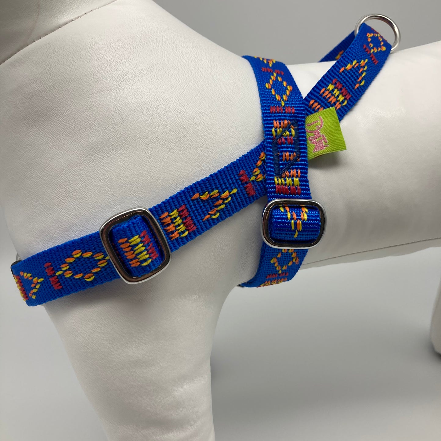 blue Stitch (blue fabric with print in 3 colors, red, yellow and orange) harness, from the side, showing the loop, the stainless steel parts and the applegreen label