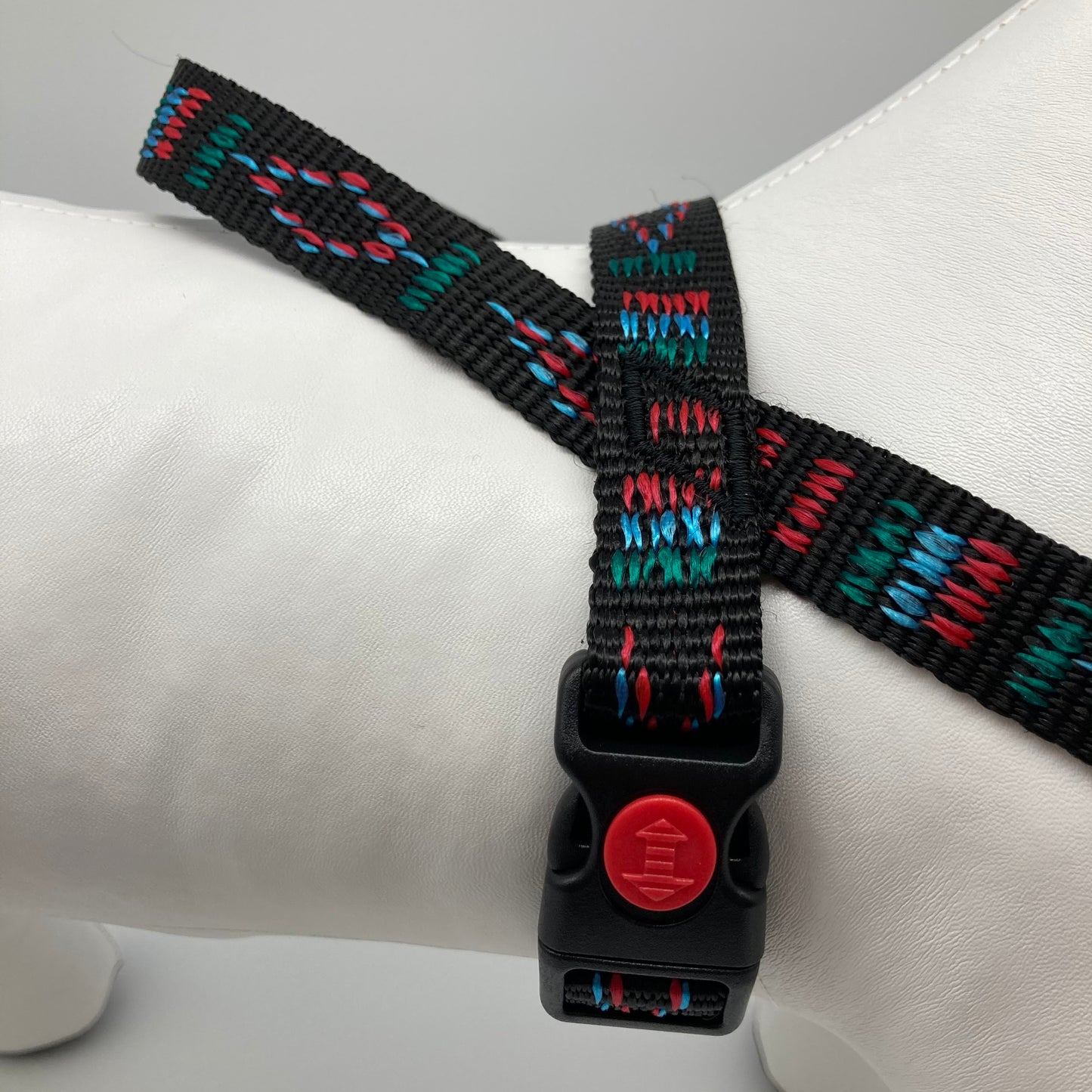 black Stitch (black fabric with print in 3 colors, red, light blue and green) harness displayed on a stuffed toy (dog), around the torso, showing the black lock and the loop on the back