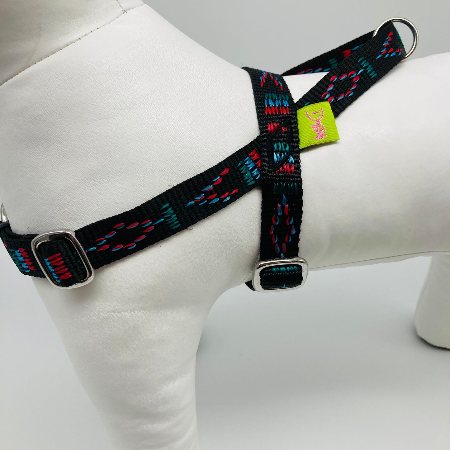 black Stitch (black fabric with print in 3 colors, red, light blue and green) harness, from the side, showing the loop, the stainless steel parts and the applegreen label