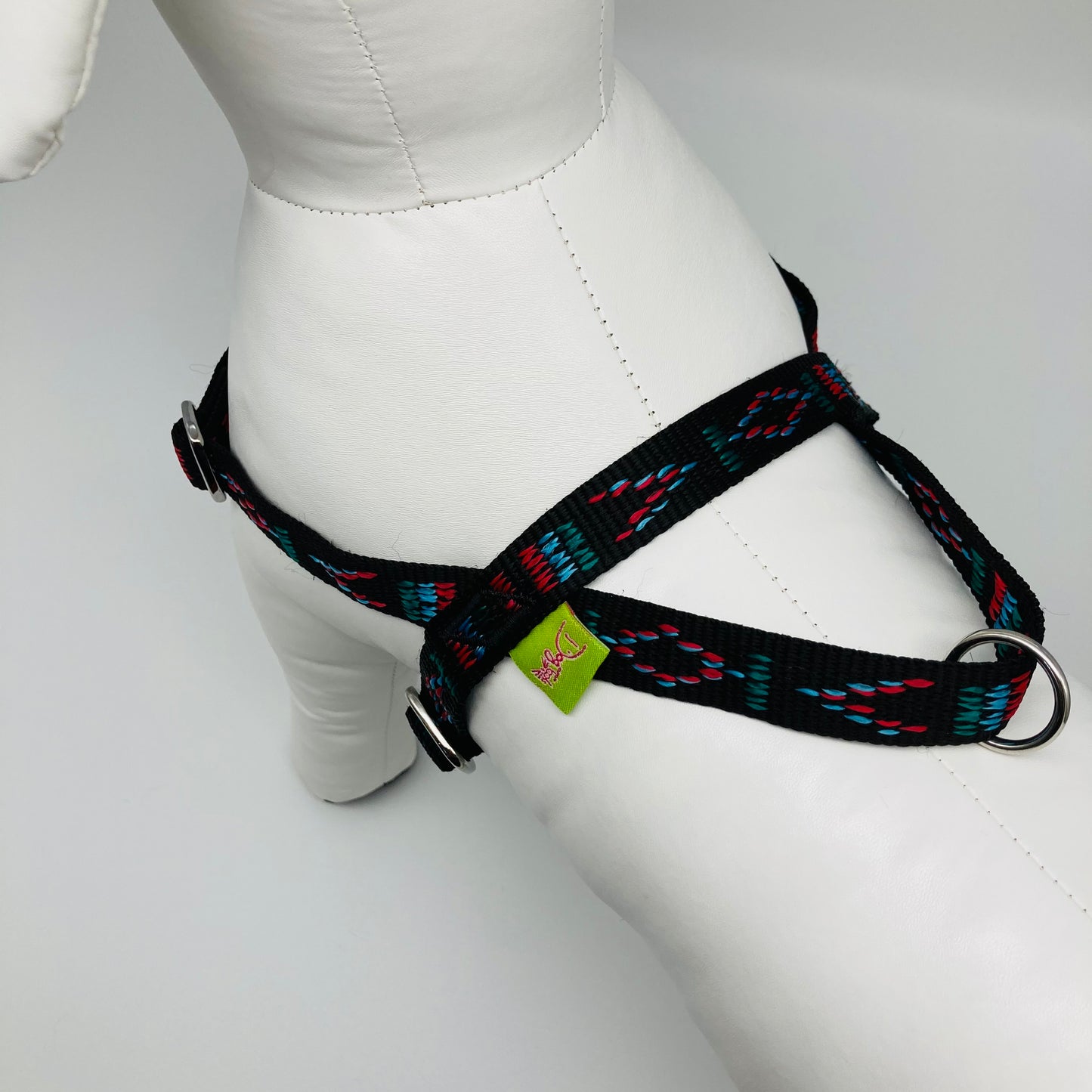 black Stitch (black fabric with print in 3 colors, red, light blue and green) harness showing the back from above, showing the loop, the stainless steel ring and the applegreen label