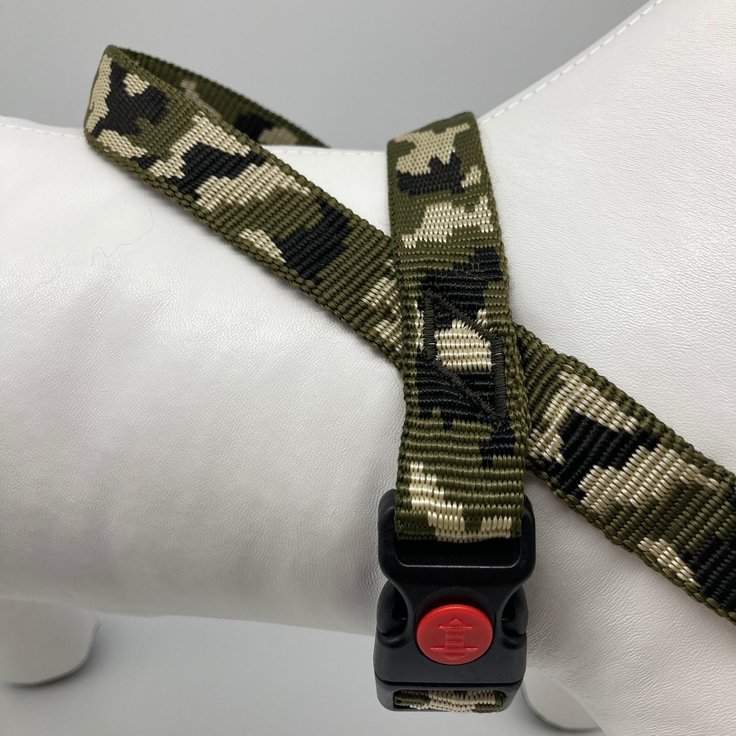 army green (army print in 3 colors, olive green, beige and black) harness, displayed on a stuffed toy (dog), around the torso, showing the black lock and the loop on the back