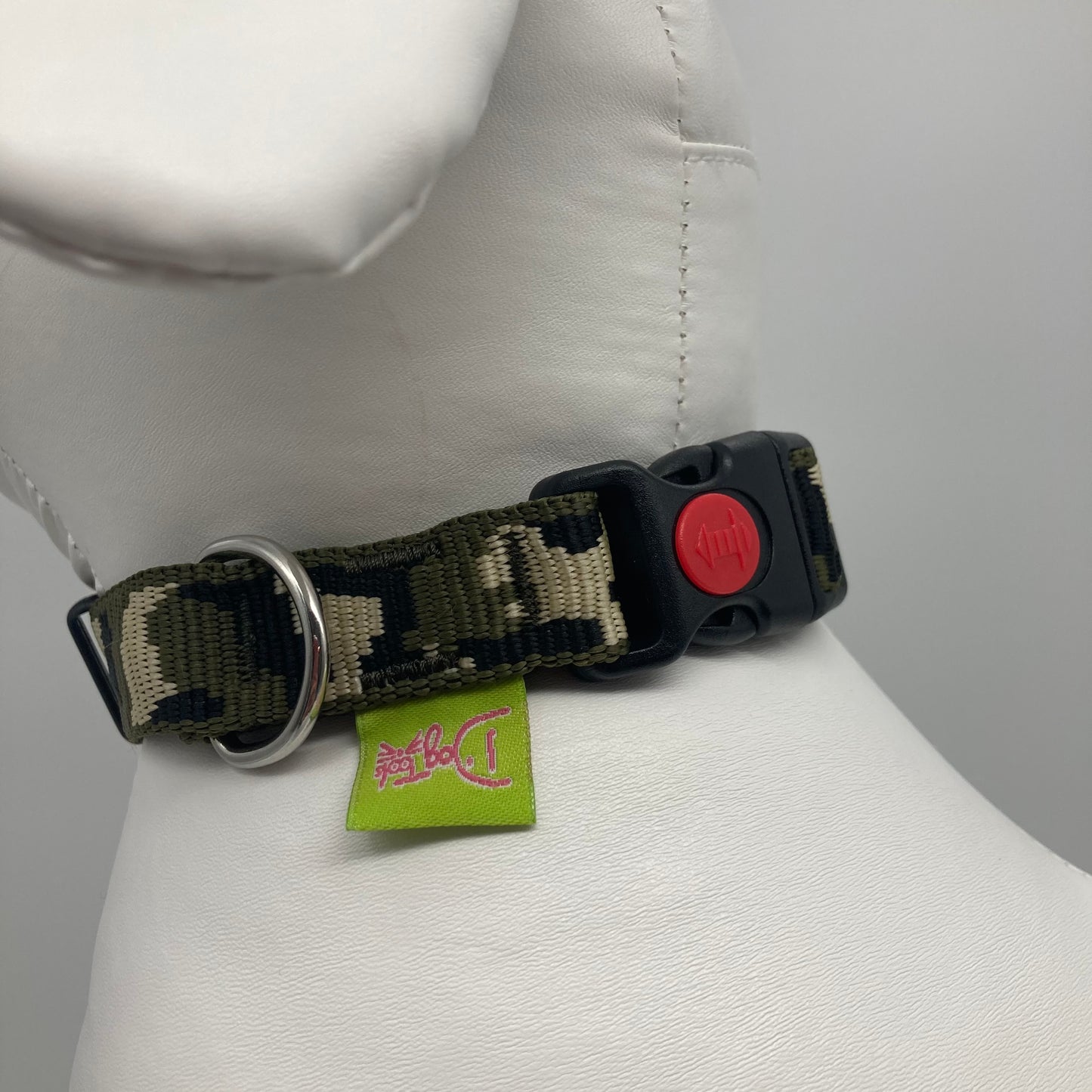 army green (army print in 3 colors, olive green, beige and black) collar showing the black lock, stainless steel ring and the applegreen label with DogTools logo on it. Displayed on a stuffed toy (dog), around the neck