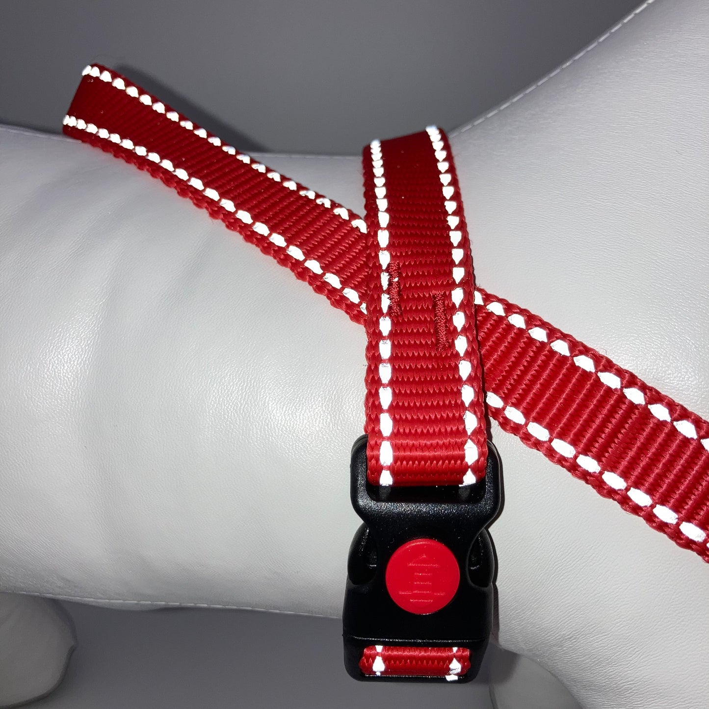 red harness with light reflecting stitches displayed on a stuffed toy (dog), around the torso, showing the black lock and the loop on the back