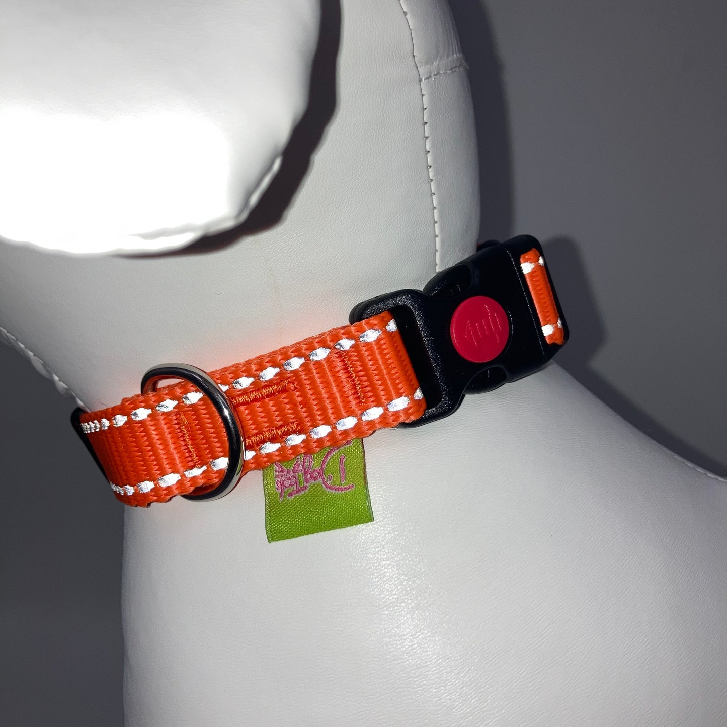 orange collar with light reflecting stitches showing the black lock, stainless steel ring and the applegreen label with DogTools logo on it. Displayed on a stuffed toy (dog), around the neck
