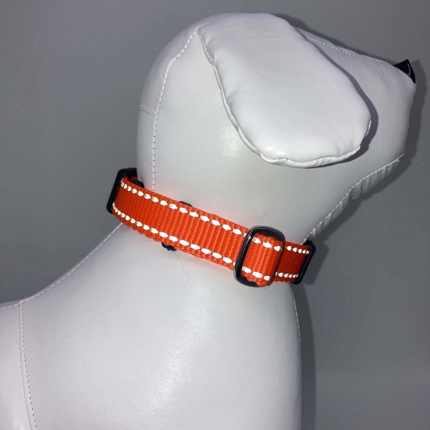 orange collar with light reflecting stitches displayed on a stuffed toy (dog), showing the back of the head and the collar from behind