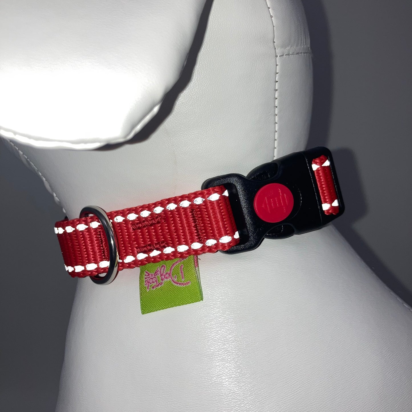 red collar with light reflecting stitches showing the black lock, stainless steel ring and the applegreen label with DogTools logo on it. Displayed on a stuffed toy (dog), around the neck