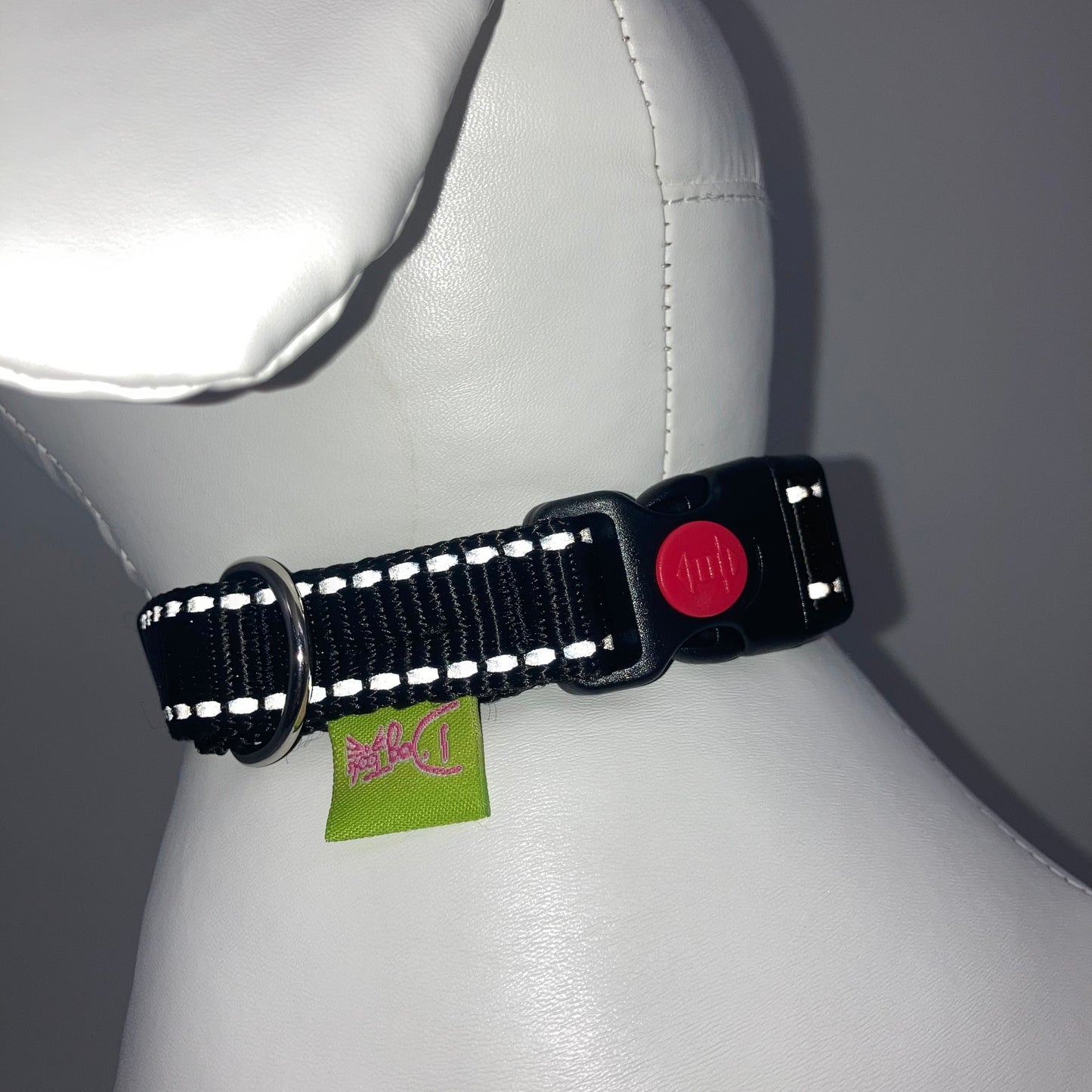 black collar with light reflecting stitches showing the black lock, stainless steel ring and the applegreen label with DogTools logo on it. Displayed on a stuffed toy (dog), around the neck