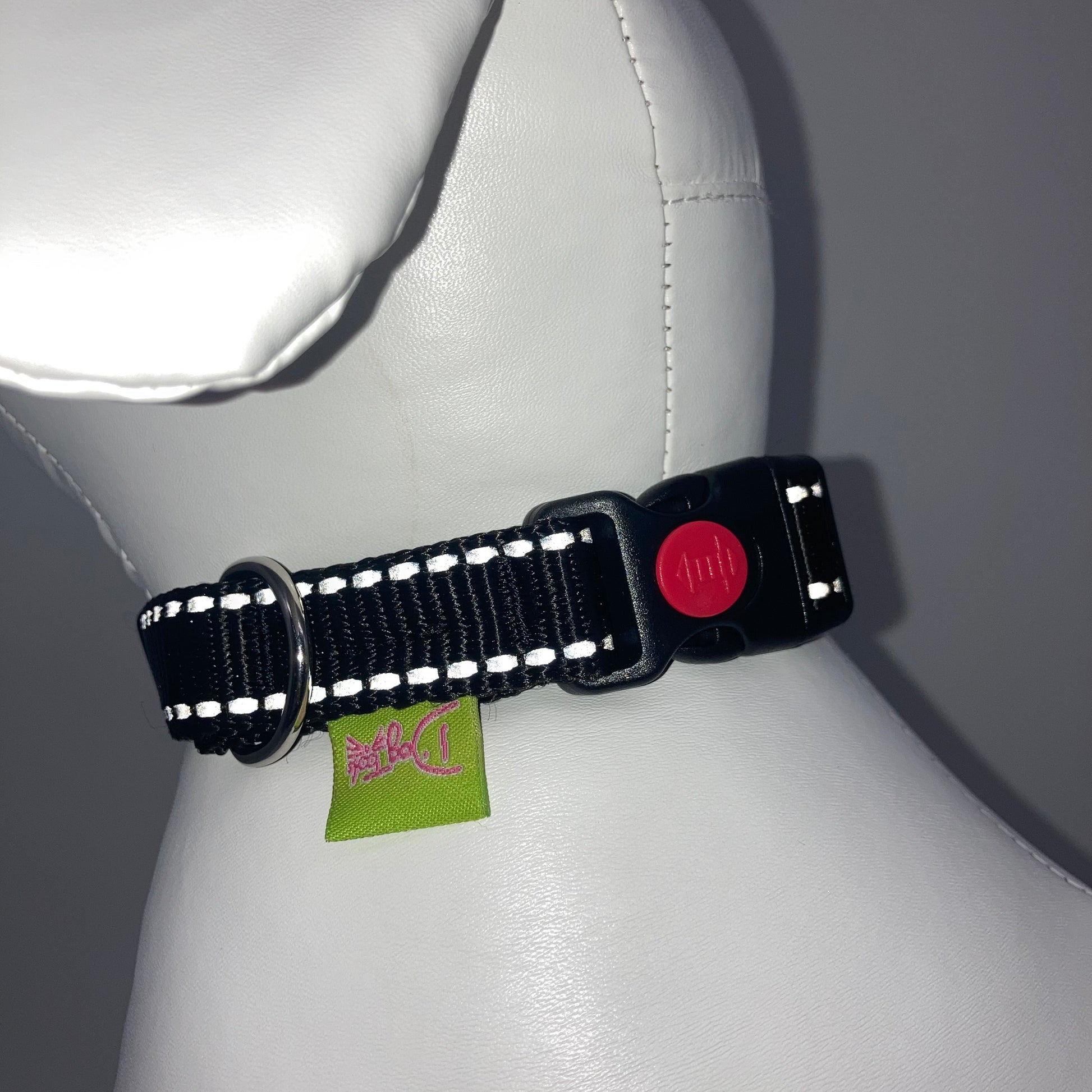 black collar with light reflecting stitches showing the black lock, stainless steel ring and the applegreen label with DogTools logo on it. Displayed on a stuffed toy (dog), around the neck