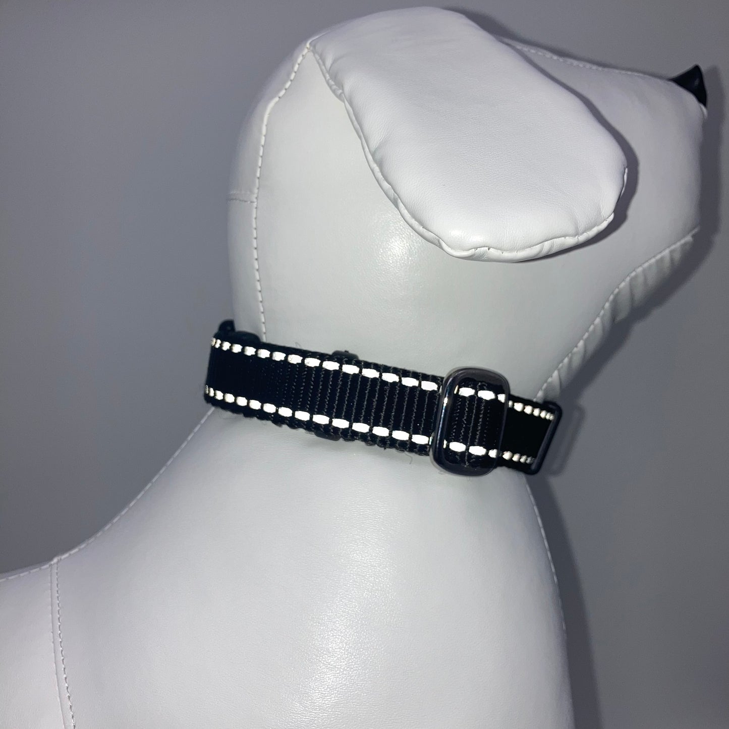 black collar with light reflecting stitches displayed on a stuffed toy (dog), showing the back of the head and the collar from behind