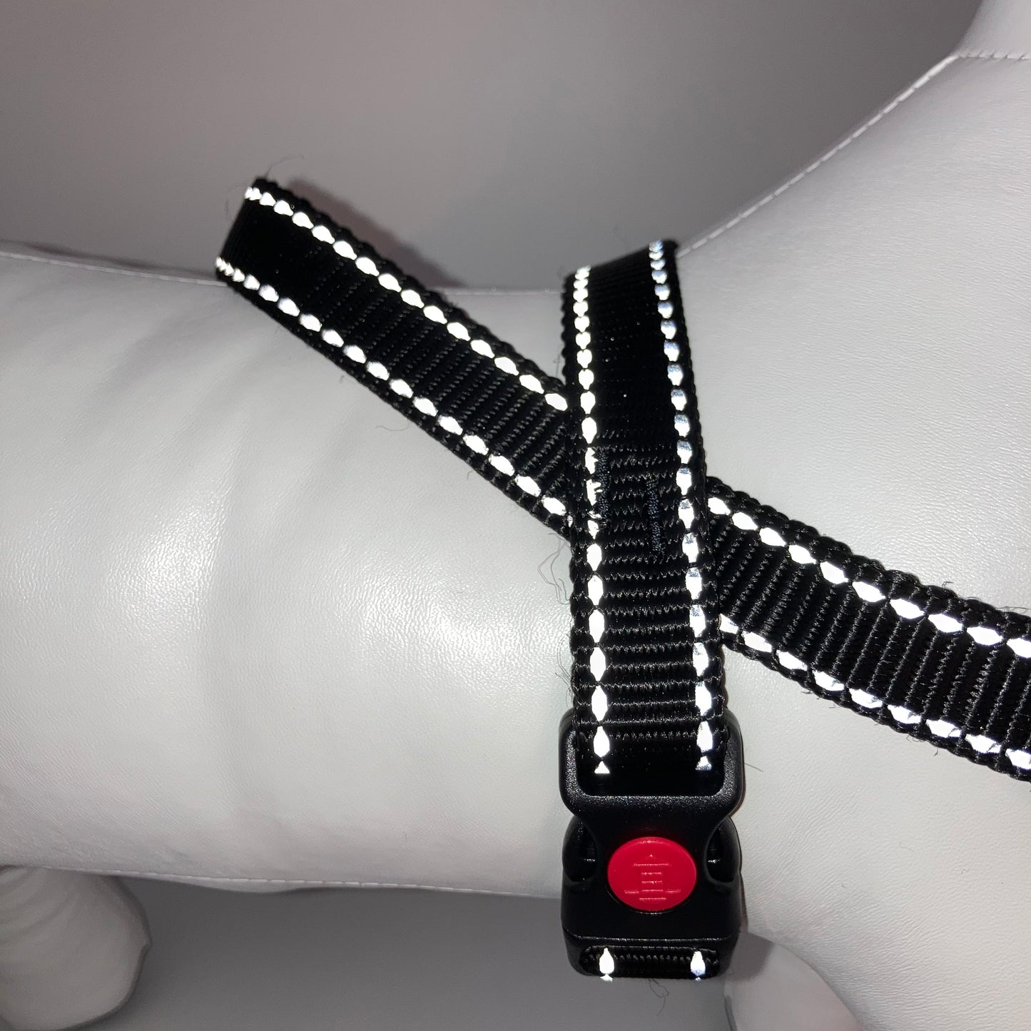 black harness with light reflecting stitches displayed on a stuffed toy (dog), around the torso, showing the black lock and the loop on the back