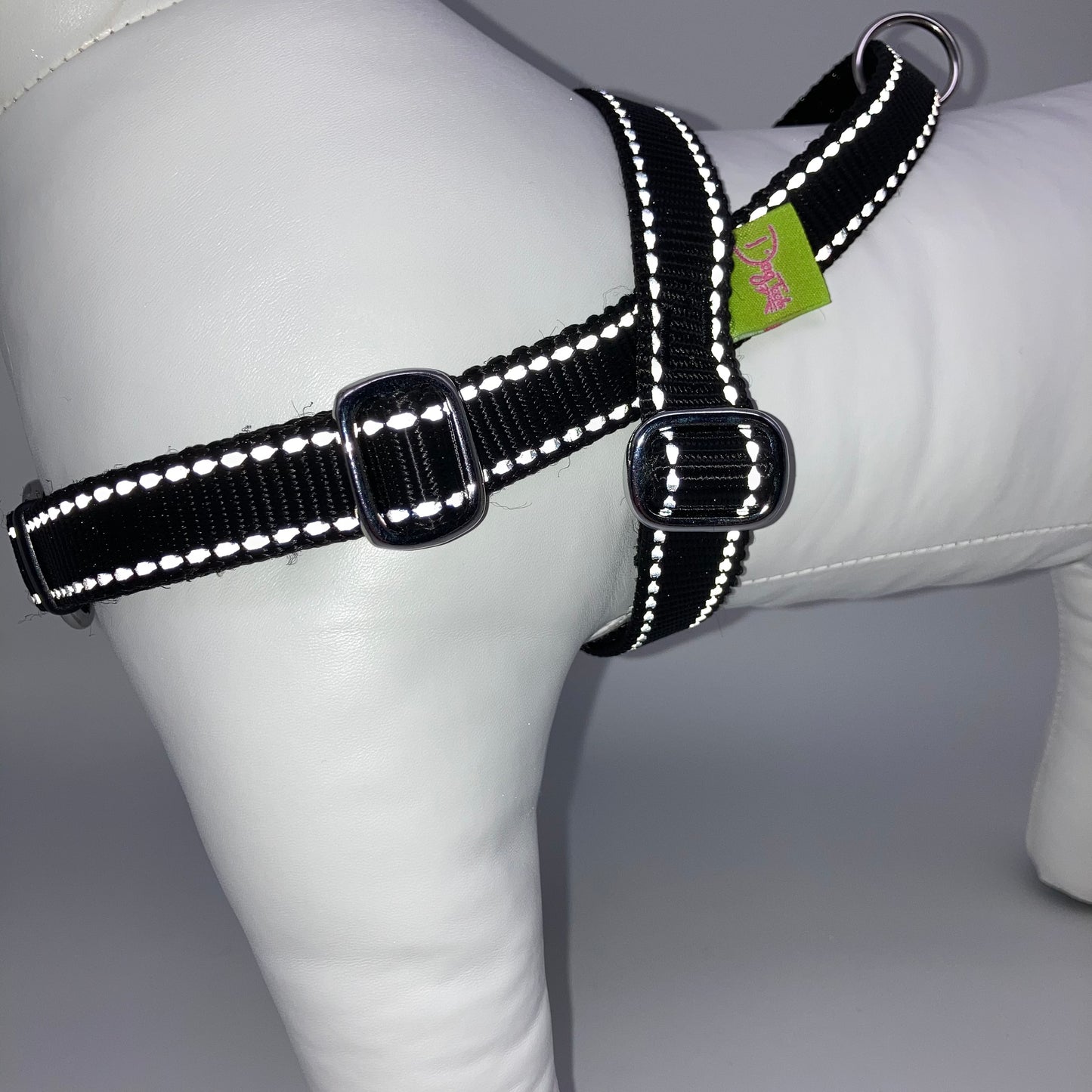 black harness with light reflecting stitches, from the side, showing the loop, the stainless steel parts and the applegreen label