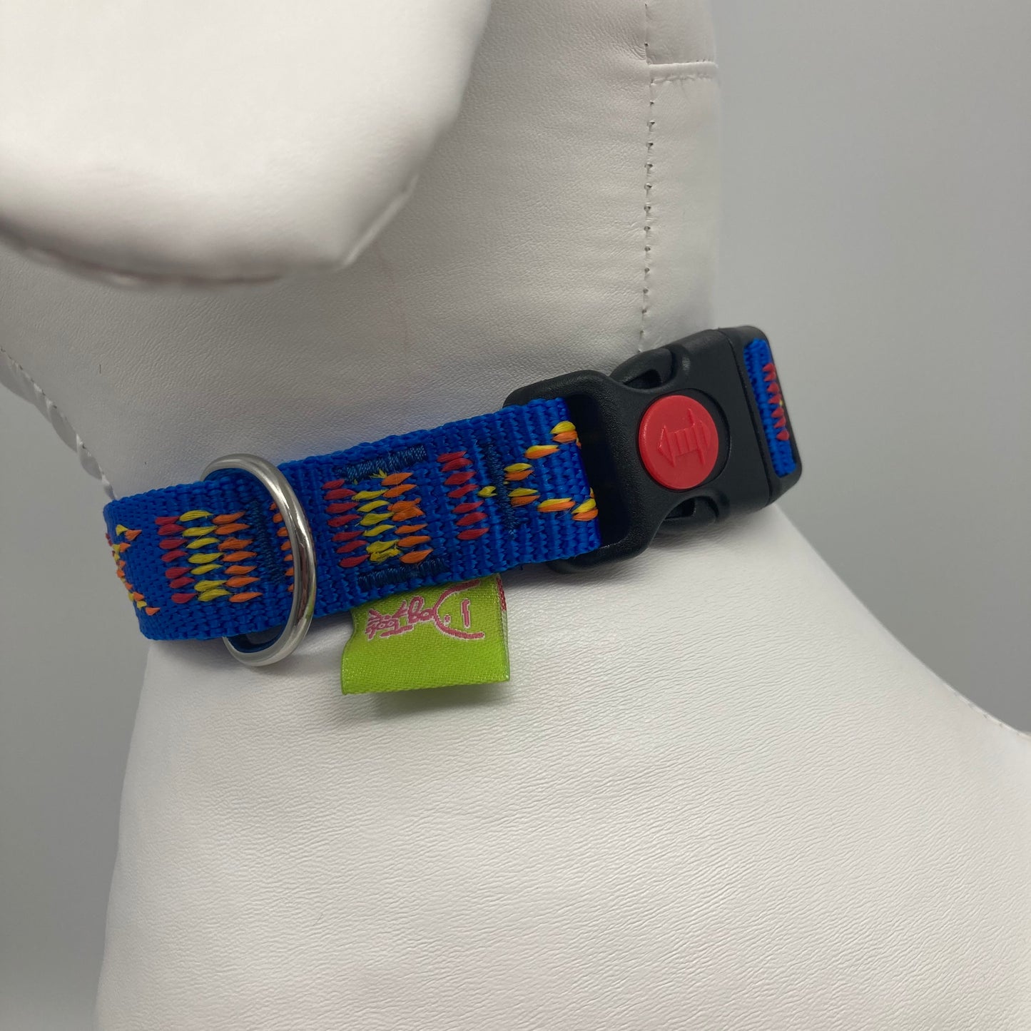 blue Stitch (blue fabric with print in 3 colors, red, yellow and orange) collar showing the black lock, stainless steel ring and the applegreen label with DogTools logo on it. Displayed on a stuffed toy (dog), around the neck