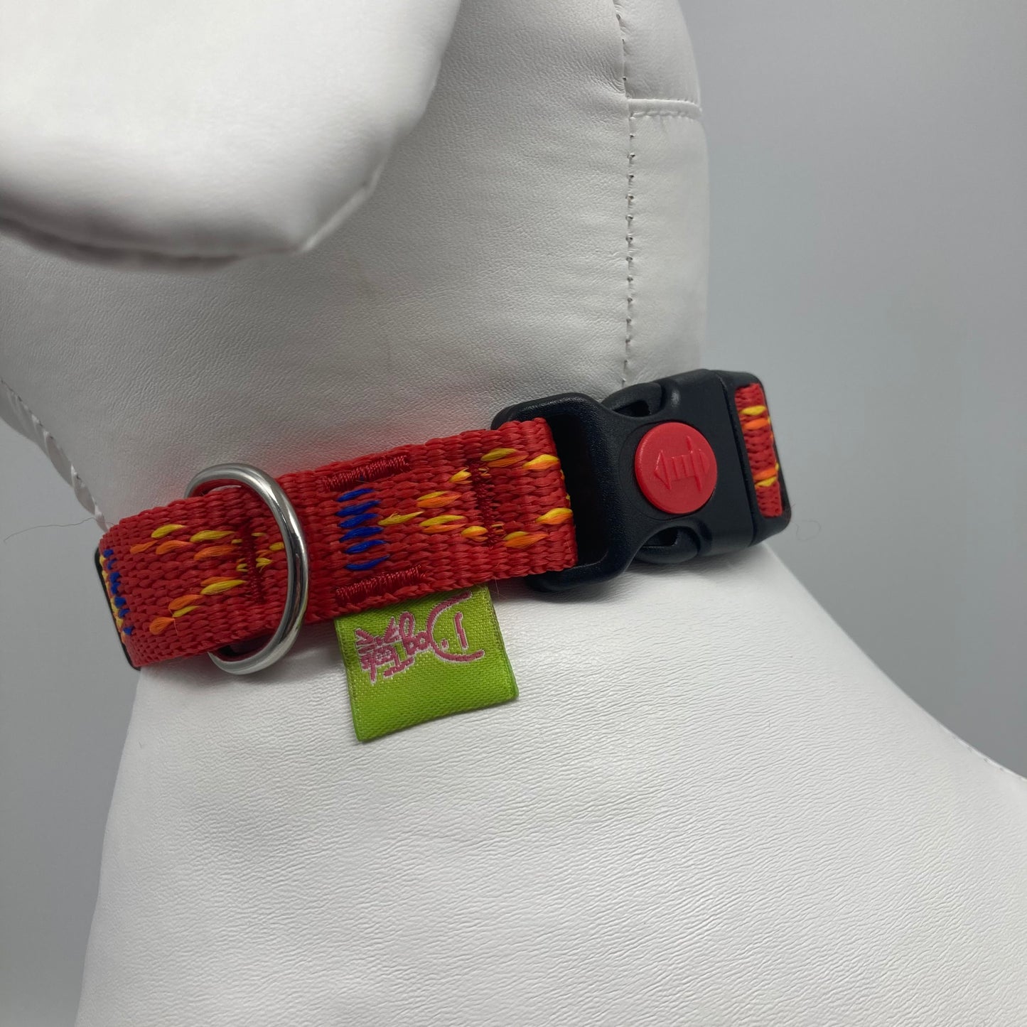red Stitch (red fabric with print in 3 colors, yellow, orange and blue) collar showing the black lock, stainless steel ring and the applegreen label with DogTools logo on it. Displayed on a stuffed toy (dog), around the neck
