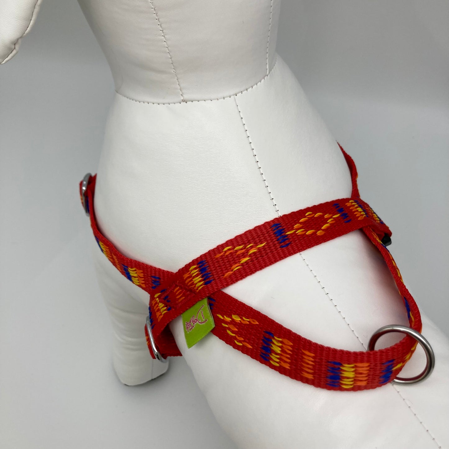 red Stitch (red fabric with print in 3 colors, yellow, orange and blue) harness showing the back from above, showing the loop, the stainless steel ring and the applegreen label