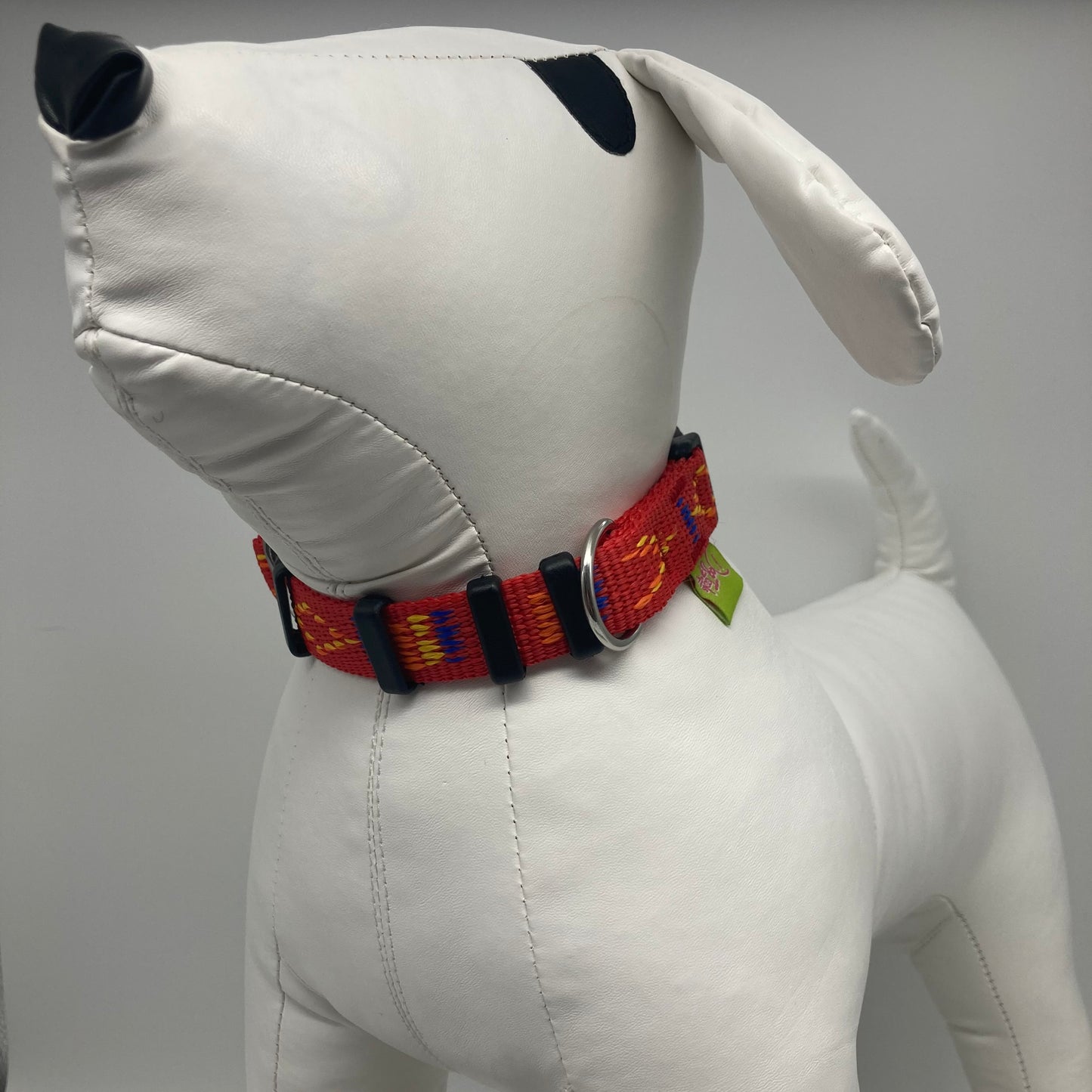 red Stitch (red fabric with print in 3 colors, yellow, orange and blue) collar displayed on a stuffed toy (dog), from the front of the dog, showing its head and torso