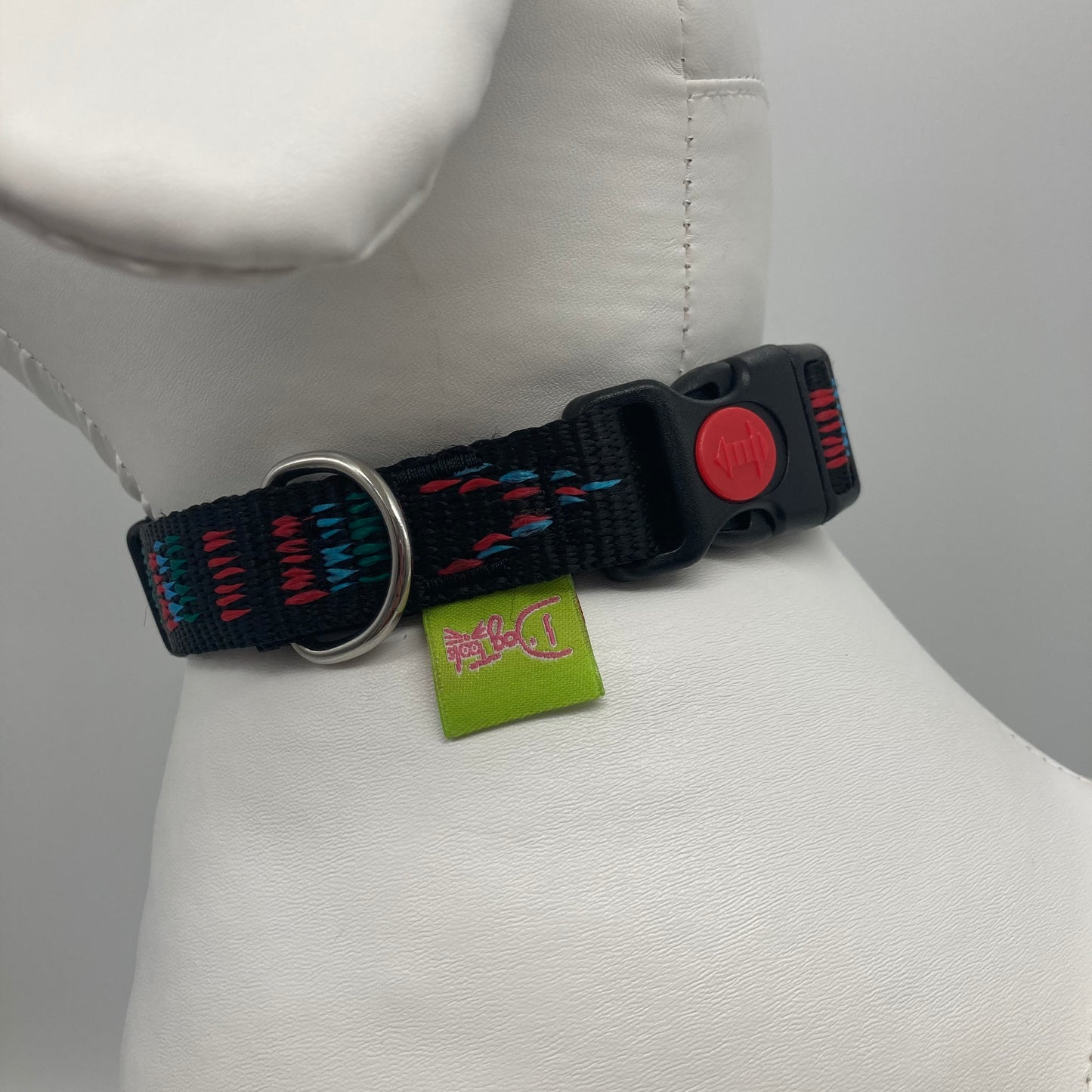 Stitch black (black fabric with print in 3 colors, red, light blue and green) collar showing the black lock, stainless steel ring and the applegreen label with DogTools logo on it. Displayed on a stuffed toy (dog), around the neck