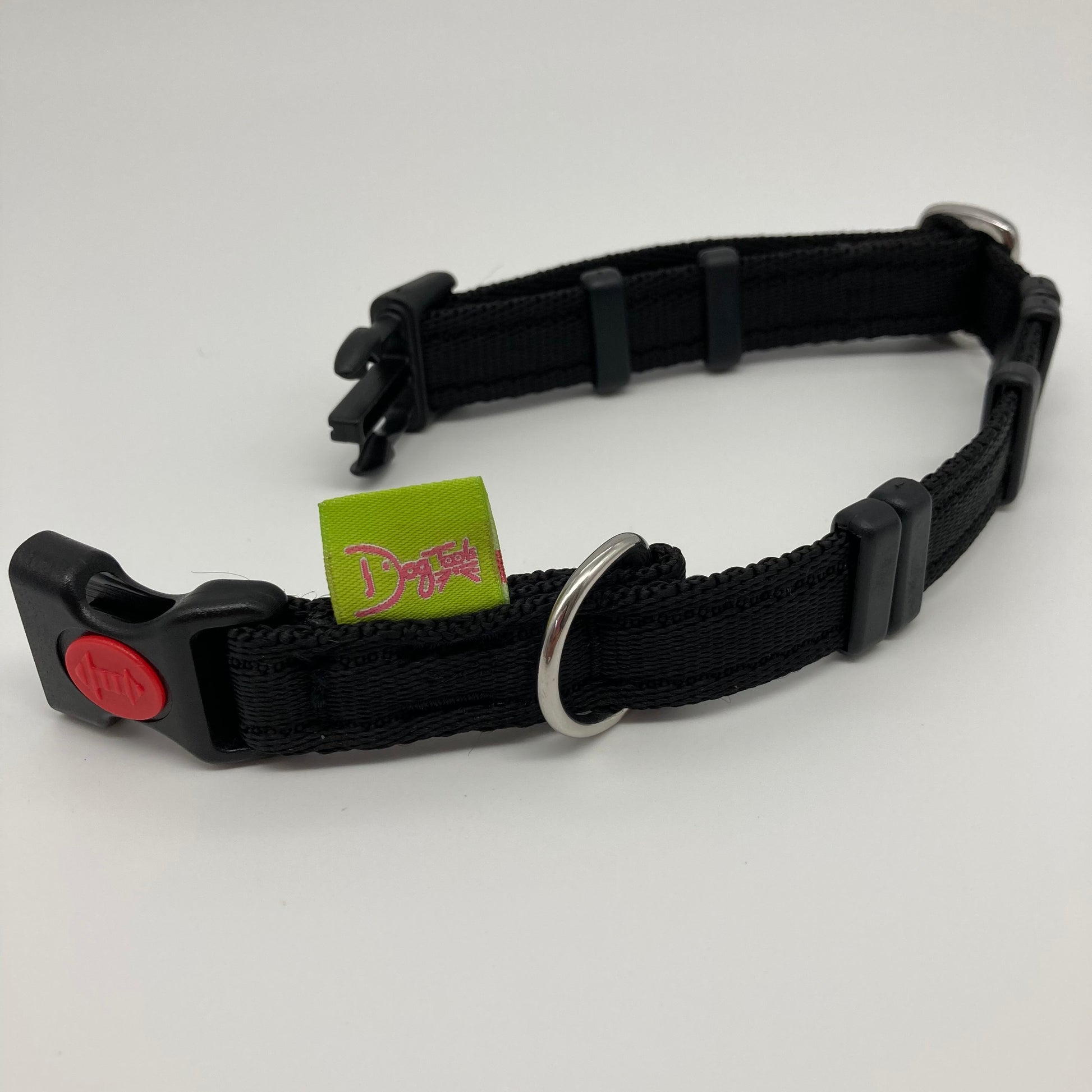 black collar displayed on a white surface, unlocked, showing the black lock, stainless steel ring, the black loops and the applegreen DogTools label