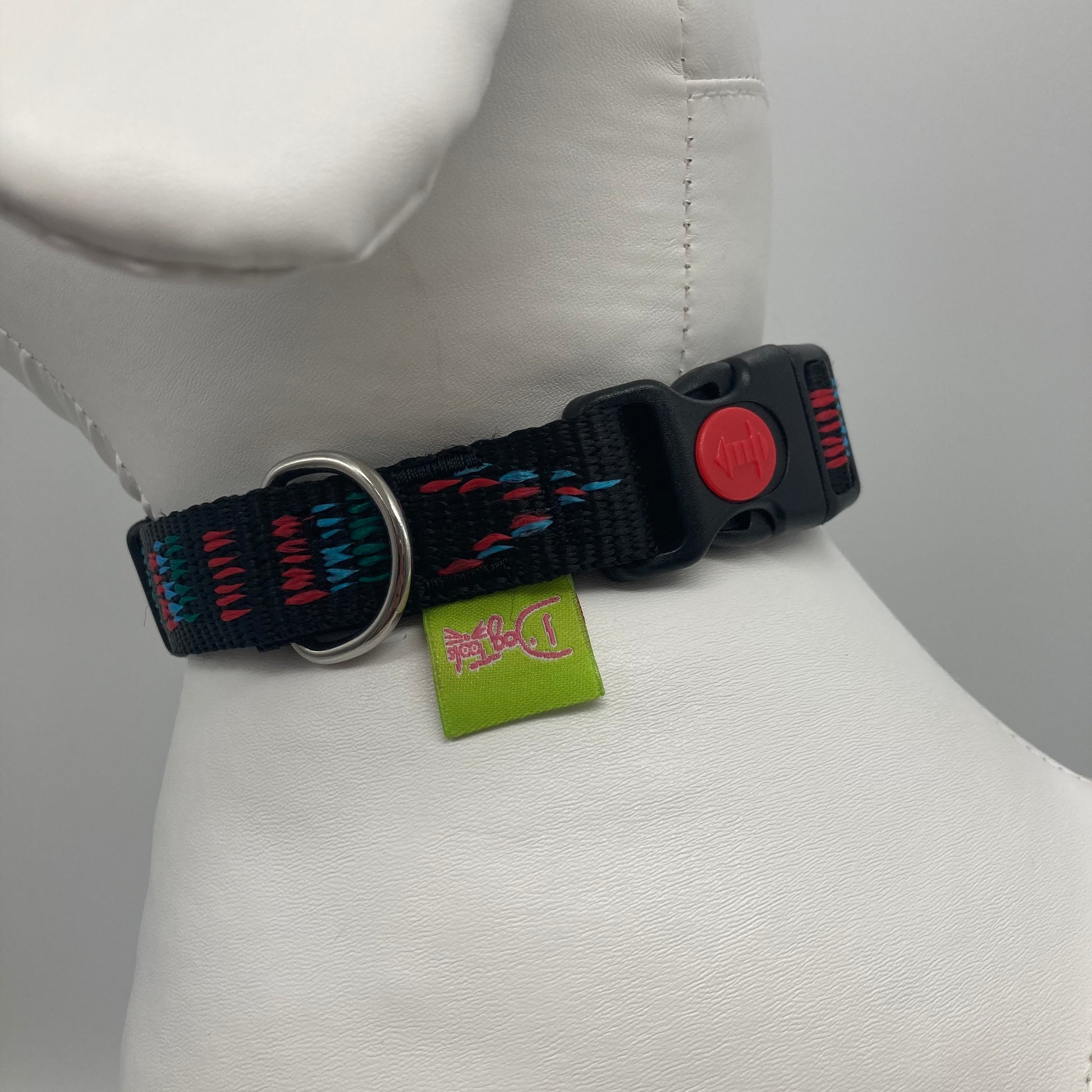 Stitch black (black fabric with print in 3 colors, red, light blue and green) collar showing the black lock, stainless steel ring and the applegreen label with DogTools logo on it. Displayed on a stuffed toy (dog), around the neck